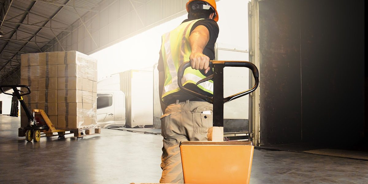 Warehouse worker unloading pallet shipment goods into a truck container, warehouse industry freight, logistics and transport.