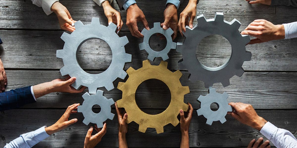 Group of business people joining together silver and golden colored gears on table at workplace top view