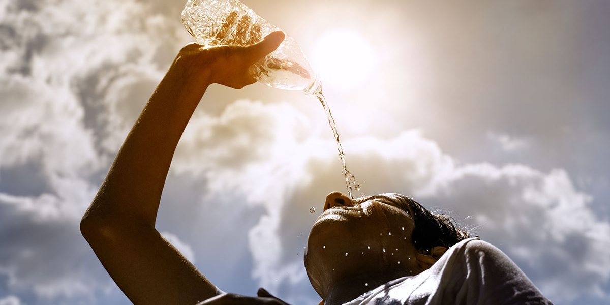 Young woman drinking fresh water from a plastic bottle under the hot summer sun