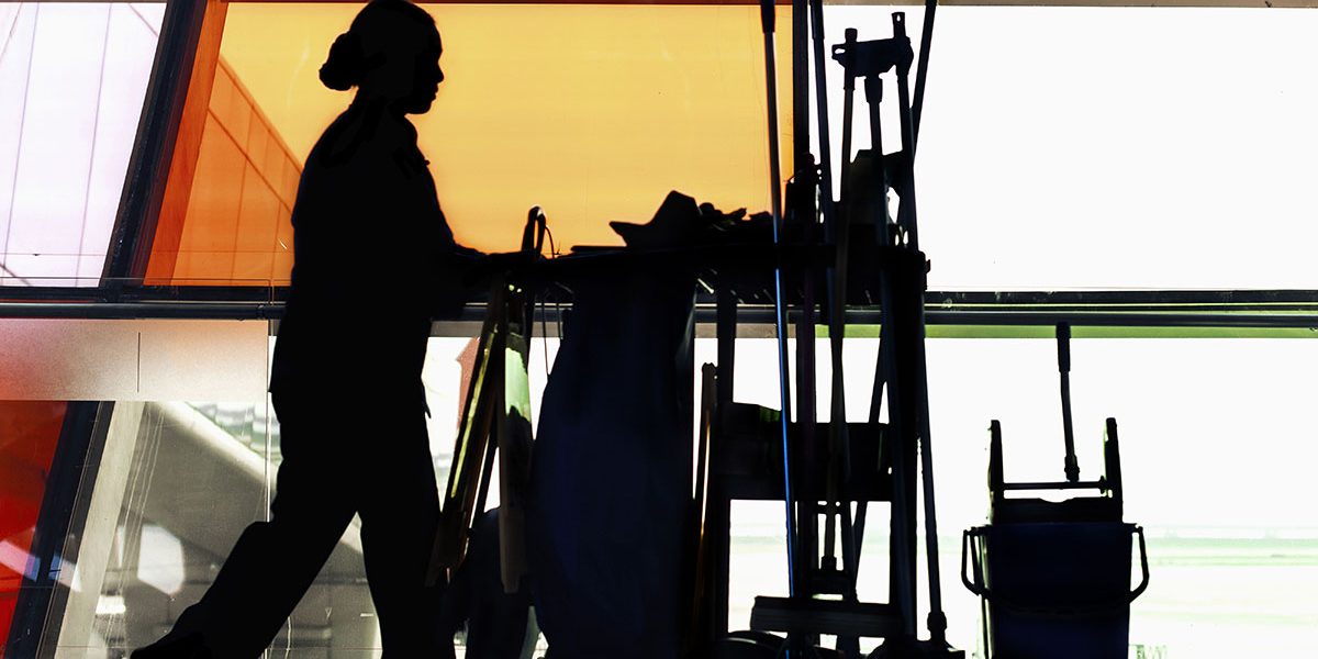 Custodian janitor pushing cleaning cart down hallway