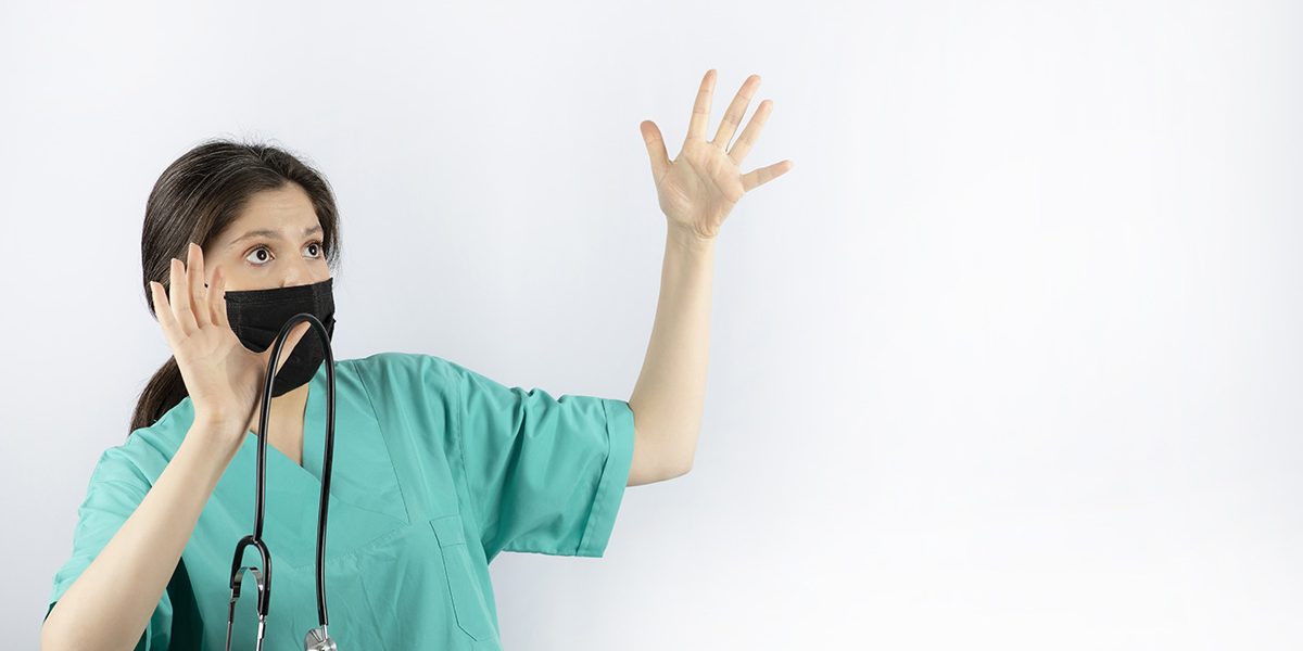 Scared young nurse holding her hands up and hold stethoscope.